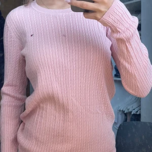 Rosa stickad tröja från Tommy Hilfiger - Säljer en snygg rosa stickad tröja från Tommy Hilfiger. Tröjan har ett klassiskt kabelstickat mönster och en liten logga på bröstet. Perfekt för en stilren look!