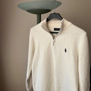 Vit Polo Ralph Lauren - Snygg vit tröja från Polo Ralph Lauren med en halv dragkedja och perfekt för en stilren look. L finns tillgänglig 