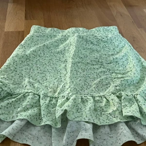 Grön blommig kjol från Gina Tricot i stl xs - Söt grön kjol från Gina Tricot med ett blommigt mönster och volangdetaljer. Perfekt för en somrig look. Kjolen har en bekväm passform och är lätt att matcha med olika toppar.