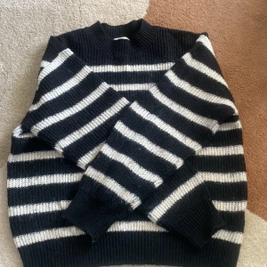 Svart och vit randig tröja från H&M - Säljer en snygg svart och vit randig tröja från H&M. Tröjan är stickad och har långa ärmar med en ribbad struktur. Perfekt för kyligare dagar och ger en stilren look. Hör av dig vid intresse!
