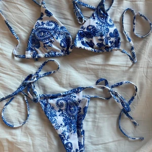 Vit och blå bikini  - Snygg bikini i vitt och blått med paisleymönster. Både överdel och underdel har knytband för justerbar passform. Helt oanvänd!!!