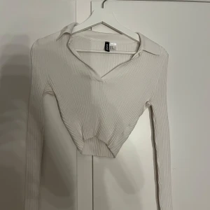  ribbad croppad tröja - Säljer en stilren vit ribbad tröja från H&M Divided. Tröjan är croppad med en v-ringad krage och långa ärmar. Perfekt för en trendig look! Och sitter välldigt fint med kroppens kurvor