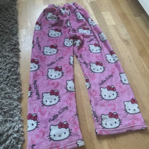 Rosa Hello Kitty mjukisbyxor - Säljer ett par rosa mjukisbyxor med Hello Kitty-motiv. Byxorna har ett elastiskt midjeband och är täckta med söta Hello Kitty-ansikten och små rosetter. Perfekta för en mysig dag hemma!🩷🩷 Passar alla storlekar och är stretchiga🩷