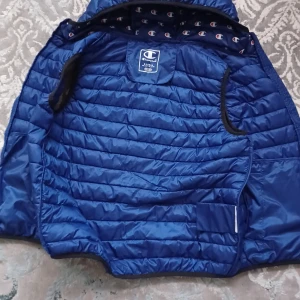 Blå väst från Champion. (Kolla beskrivningen) - Säljer en blå quiltad dunväst från Champion. Västen har en huva och är perfekt för kyligare dagar. Den är lätt och smidig att bära, med ett stilrent mönster och Champion-loggan på insidan av luvan. Passar dig som är ca 158cm, 12-14 år. Inga defekter på västen. Västen är använd 2 gånger och är i mycket bra skick.