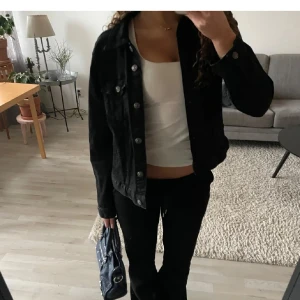 Svart jeansjacka - Snygg svart jeansjacka med knappar framtill och klassisk krage. Perfekt för en casual look och lätt att matcha med olika outfits. Jackan har långa ärmar och två bröstfickor med knappstängning. (Det är inte jag på bilden!!!) Men den är i bra skick och är köpt för 250kr 