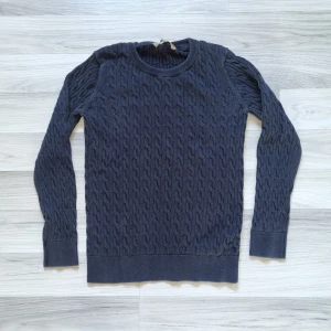 Svart stickad tröja från Basic U - Säljer en stilren svart stickad tröja från Basic U. Tröjan har ett klassiskt flätmönster och långa ärmar. Den är mjuk och bekväm med ribbade muddar vid ärmslut och nederkant.