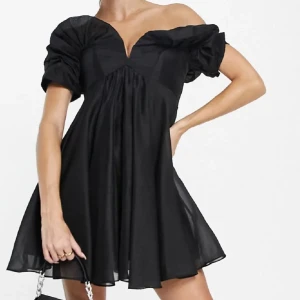 Svart kortklänning med puffärmar - Säljer en elegant svart kortklänning med puffiga offshoulder-ärmar och v-ringning. Perfekt för en utekväll eller speciella tillfällen. Klänningen har en luftig passform och är tillverkad i ett lätt material som ger en fin rörelse. (Klänningen är utstruken på mina biler.) Passad s/m