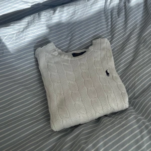 Vit stickad tröja från Ralph Lauren - Säljer en stilren vit stickad tröja från Ralph Lauren med klassiskt flätmönster. Tröjan har långa ärmar och en liten broderad logotyp på bröstet. Perfekt för en elegant och avslappnad look. Nypris 2295 kr