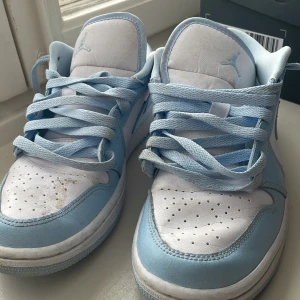 Nike Air Jordans i ljusblått och vitt - Snygga Nike Air Jordans i en fräsch ljusblå och vit färgkombination. Skorna har klassisk snörning och en ikonisk design med Air Jordan-loggan på hälen. Perfekta för dig som vill ha en stilren look.