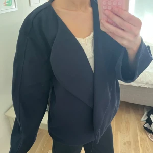 Mörkblå kappa - Snygg mörkblå kappa med en stilren design. Den har en lös passform och långa ärmar, perfekt för en elegant look. 