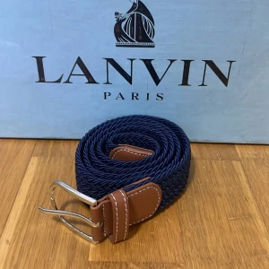 Blått flätat bälte - Snyggt blått flätat bälte med bruna skinn-detaljer och en stilren silverfärgad spänne. Perfekt för att ge en elegant touch till din outfit. Passar både till jeans och mer formella byxor. Helt nytt!