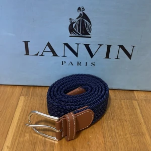 Blått flätat bälte  - Snyggt blått flätat bälte med bruna läderdetaljer och ett stilrent silverfärgat spänne. Perfekt för att ge en elegant touch till din outfit. Kommer i originalförpackning. Helt nytt!