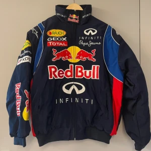 Red Bull racingjacka - Snygg blå racingjacka från Red Bull med flera logotyper, inklusive Infiniti och Pepe Jeans. Jackan har en dragkedja framtill och är dekorerad med röda och gula detaljer. Perfekt för racingfans som vill sticka ut. Pris kan diskuteras. Kan passa bra på någon med en mindre storlek som S & M.
