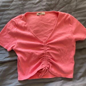 Rosa ribbad topp från FB Sister - Säljer en söt rosa ribbad topp från FB Sister i storlek M. Toppen har en v-ringning och korta ärmar med en snygg knytdetalj framtill. 🩷