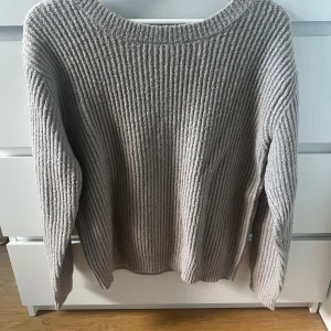 Grå ribbad tröja från NA-KD - Säljer en stilren grå ribbad tröja från NA-KD. Tröjan har en v-ringad design i ryggen och långa ärmar, perfekt för kyligare dagar. Den är i storlek XS och passar utmärkt för en avslappnad look.