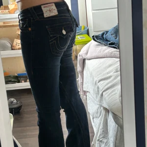 True Religion Joey Low Rise Flare Jeans - Snygga mörkblå jeans från True Religion med låg midja och flare-stil. De har en klassisk femficksdesign med märkets ikoniska broderi på bakfickorna och en knappdetalj. Perfekta för en avslappnad och trendig look. Mått: innerbenslängd 79cm, midja tvärs över 39cm | när jag köpte dom så var dom för långa så har fått dom uppsydda så kolla räkna med nya mått och kvitto finns kvar ifall bild önskas. 