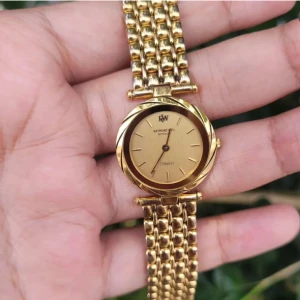 Guldfärgad klocka från Raymond Weil - Elegant guldfärgad klocka från Raymond Weil med en klassisk rund urtavla och matchande armband. Perfekt för den som vill ha en tidlös accessoar med stilren design. Urtavlan har subtila markeringar och märket är tydligt synligt.