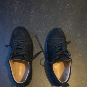 Svarta sneakers från Christian Louboutin - Snygga svarta sneakers i mocka från Christian Louboutin med den ikoniska röda sulan. Skorna har snörning och en stilren design som passar perfekt för en trendig look.