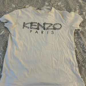 Vit t-shirt från Kenzo - Säljer en vit t-shirt från Kenzo med tryck 'KENZO PARIS' i svart på framsidan. T-shirten har korta ärmad.