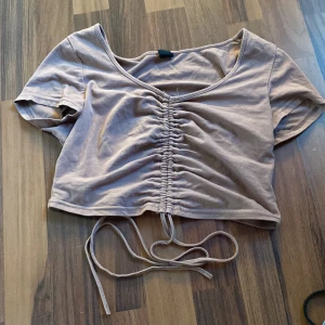 Beige croppad topp med knyt - Säljer en beige croppad topp med korta ärmar och knytning framtill. Toppen har en v-ringad design och är perfekt för en trendig look.