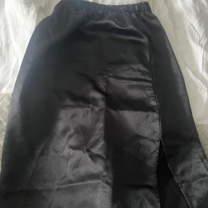 Svart kjol från Parisian - Elegant svart kjol från Parisian med en stilren slits framtill. Kjolen har en elastisk midja för bekväm passform och är tillverkad i ett glansigt material som ger en lyxig känsla.