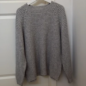 Grå stickad tröja från Lager 157 - Säljer en mysig grå stickad tröja från Lager 157. Tröjan har en klassisk rund hals och långa ärmar, perfekt för kyliga dagar. Den har en fin textur och ribbstickade muddar vid ärmslut och nederkant.