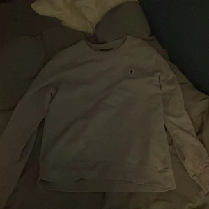 Grå tröja från Morris  - Säljer en stilren grå tröja från Morris Stockholm med ett broderat emblem på bröstet. Tröjan har långa ärmar och en klassisk rund halsringning. Perfekt för en avslappnad och snygg look. Priset är ej hugget i sten! 