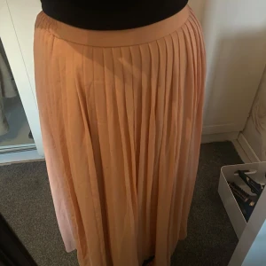 Plisserad långkjol i ljusrosa - Säljer en snygg plisserad långkjol i ljusrosa färg. Kjolen har ett brett midjeband och faller fint ner längs benen. Perfekt för dig som vill ha en flowy och trendig look.