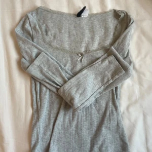 Grå långärmad topp från H&M Divided - Säljer denna super gulliga gråa långärmade topp från H&M Divided. Den har en söt spetskant och en liten rosett vid halsringningen. Perfekt för både vardag och fest! 😍💓💓