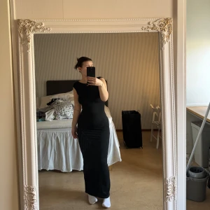 Svart långklänning med öppen rygg - Elegant svart långklänning med en stilren design och öppen rygg. Klänningen har en tight passform som framhäver figuren. Perfekt för en kväll ute eller en speciell tillställning.