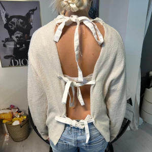 Beige tröja med öppen rygg och knytband - Säljer en beige tröja med unik design. Tröjan har en öppen rygg med flera knytband som ger en snygg detalj. Den är långärmad och har en mjuk, bekväm passform. Perfekt för att sticka ut med stil!