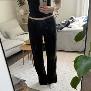 Svarta kostymbyxor med normal passform - Säljer ett par klassiska svarta kostymbyxor med normal passform och lite vidare ben. Byxorna har medelhög midja och stängs med dragkedja och knapp framtill. Perfekta till både vardagliga och mer uppklädda tillfällen. Storlek 36 och längden är regular.