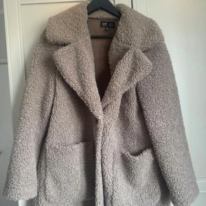 Beige teddyjacka från Zara - Mysig beige teddyjacka från Zara TRF Collection. Jackan har en oversized passform med stora fickor framtill och en bred krage. Perfekt för kyliga dagar när du vill hålla dig varm och stilren.
