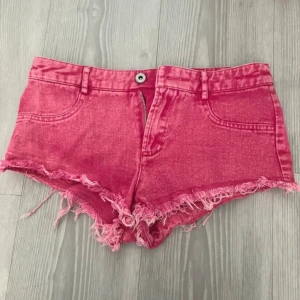 Rosa jeansshorts med fransar - Snygga rosa jeansshorts med fransig kant nertill och klassisk femficksdesign. De har knapp och dragkedja framtill samt låg midja. Perfekta för sommardagar och festivaler.