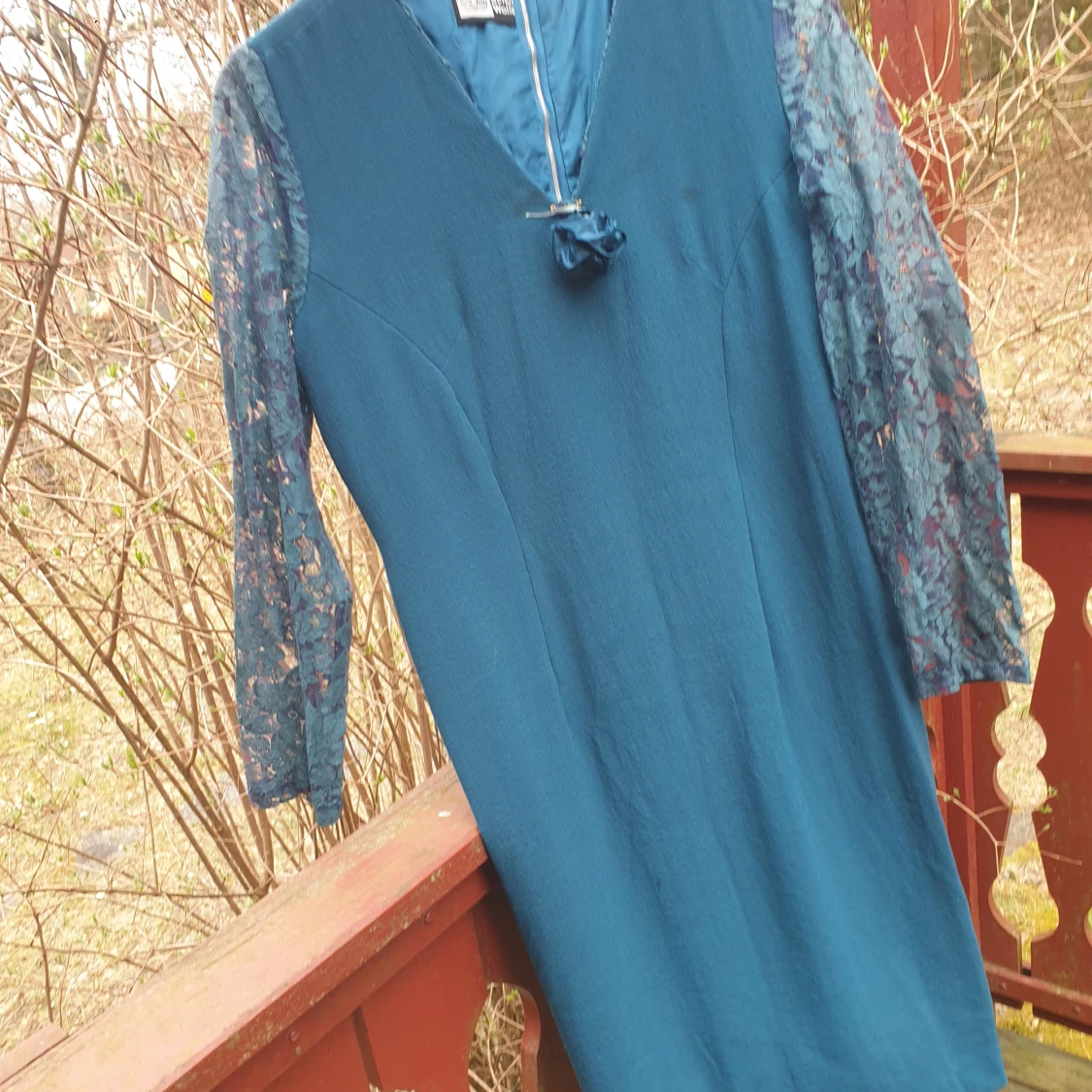 Petrolblå klänning med spetsärmar och rosettdetalj