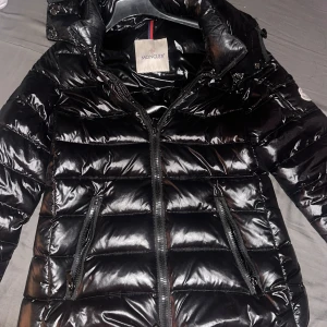 Svart dunjacka från Moncler - Säljer en glansig svart dunjacka från Moncler med huva och dragkedja framtill. Jackan har två fickor med dragkedja och Moncler-logga på ärmen. Perfekt för kyliga dagar och ger en snygg, sportig look. Äkta Moncler köpt 2024, användning 3 gånger. Storlek 01=S. köpte den för 14000kr och säljer den för 7500kr vid snabb köp kan priset diskuters. Bara seriösa kunder.