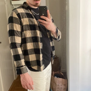 Rutig skjorta från H&M i svart och beige - Säljer en snygg rutig skjorta från H&M i svart och beige. Skjortan har långa ärmar, klassisk krage och knäppning framtill. Perfekt att bära öppen över en t-shirt eller stängd för en mer klassisk look.