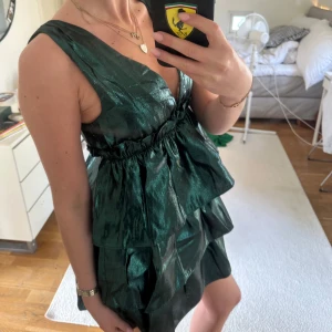 Grön glittrig volangklänning med v-ringning - grön klänning från Zara med glittrigt tyg och flera volanger. Djup v-ringning och ärmlös design, Kort modell med markerad midja