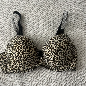 Leopardmönstrad bh med glittriga axelband - Saljer ny BH - storlek 75B, aldrig anvand! Stilren och snygg leopardmönstrad BH i mycket fint skick - helt ny och aldrig anvand. Axelbanden r avtagbara, sả den kan bäras pả flera olika sätt - perfekt under kläder med bara axlar!