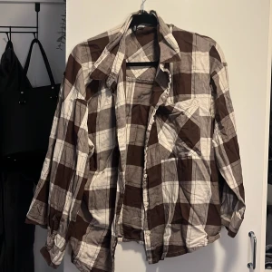 Brun och vit rutig skjorta - Säljer en brun och vit rutig skjorta med klassisk krage och bröstficka. Skjortan har långa ärmar och knäppning framtill. Perfekt för en avslappnad stil.