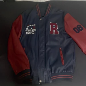 Blå och röd varsityjacka med bokstaven R - Snygg varsityjacka i blått med röda ärmar och detaljer. Stor bokstav R på bröstet, broderad text och siffran 08 på ena ärmen. Jackan har dragkedja, ribbade muddar och två fickor framtill. Perfekt för en sportig och trendig look. Har inte använts mer än en gång och storlek som står på den är XXL men det är inte EU storlek få den kan passa på m-L. Beroende på hur lång man är.