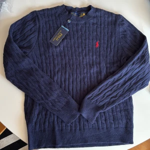 Ralph lauren stickad tröja - Säljer en mörkgrå kabelstickad tröja från Polo Ralph Lauren med rund halsringning och röd broderad logga på bröstet. 10/10 kvalité, endast testad på. Hör av er vid minsta intresse🤩🌟