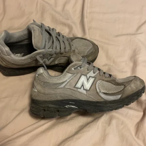  New Balance 2002r - Säljer ett par grå New Balance sneakers med klassisk N-logga på sidan. Skorna har snörning, meshpaneler för extra ventilation och en robust svart sula. Perfekta för dig som gillar en sportig och stilren look.