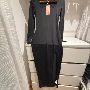 Svart långklänning med slits från SHEIN - Säljer en svart långklänning från SHEIN med lång ärm och rundad urringning. Klänningen har en snygg slits framtill som ger en extra touch. Perfekt för dig som gillar en tight passform och stilren look.