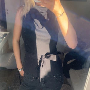 Svart ärmlös topp med knyt i midjan - Snygg svart ärmlös topp med knytband i midjan som ger en markerad siluett. Perfekt till jeans eller kjol för en stilren look. Enkel och stilren design utan synliga mönster eller detaljer.