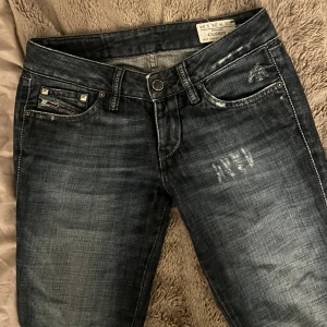 Lågmidjade  jeans - Blå lågmidjade jeans från Diesel med slitningar och nitar på fickorna. Säljer pga för små (därav kan jag inte ta några bilder med dem på)💞Snygga detaljer på bakfickorna och en cool tvättad look, är uppsprättade längst ner💞             Midjemått: 35cm                                                           Innerbenslängd: 79cm