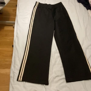 Svarta byxor med ränder från Lindex - Säljer ett par svarta byxor från Lindex med vita ränder längs sidorna. Byxorna har en loose passform och är perfekta för en avslappnad stil. De är tillverkade i ett mjukt material som ger en bekväm känsla hela dagen.