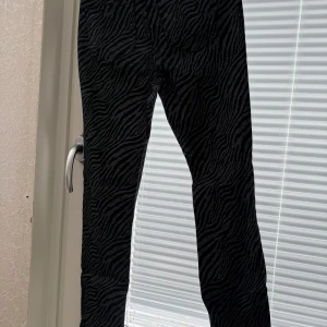 Svarta zebramönstrade byxor - Snygga svarta byxor med zebramönster. Perfekta för att ge din outfit en cool touch. Byxorna har en tight passform och är tillverkade i ett bekvämt material.