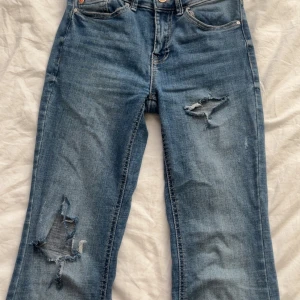 Blå jeans med slitningar - Snygga blå jeans med slitningar på båda benen. De har en klassisk femficksdesign och knappgylf. Perfekta för en avslappnad stil.