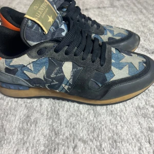 Valentino Rockrunner sneakers med stjärnmönster - Snygga Valentino Rockrunner sneakers med ett coolt camouflagemönster i blått och grått. Skorna har svarta snören och en unik stjärndetalj på hälen med nitar och en turkos accent. Perfekta för att ge din outfit en edgy touch. Dessa bilder är från när jag köpte dem men nu har jag använt dessa i cirka ett år så skicket är betydligt sämre. Flertals defekter osv men inget som märks särskilt mycket vid användning. Fråga om bilder innan så du vet skick!! Plus en defekt i hällen!!